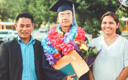 a college graduate in their cap and gown with their parents